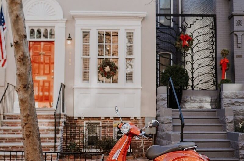 red and black motor scooter parked beside white concrete building during daytime